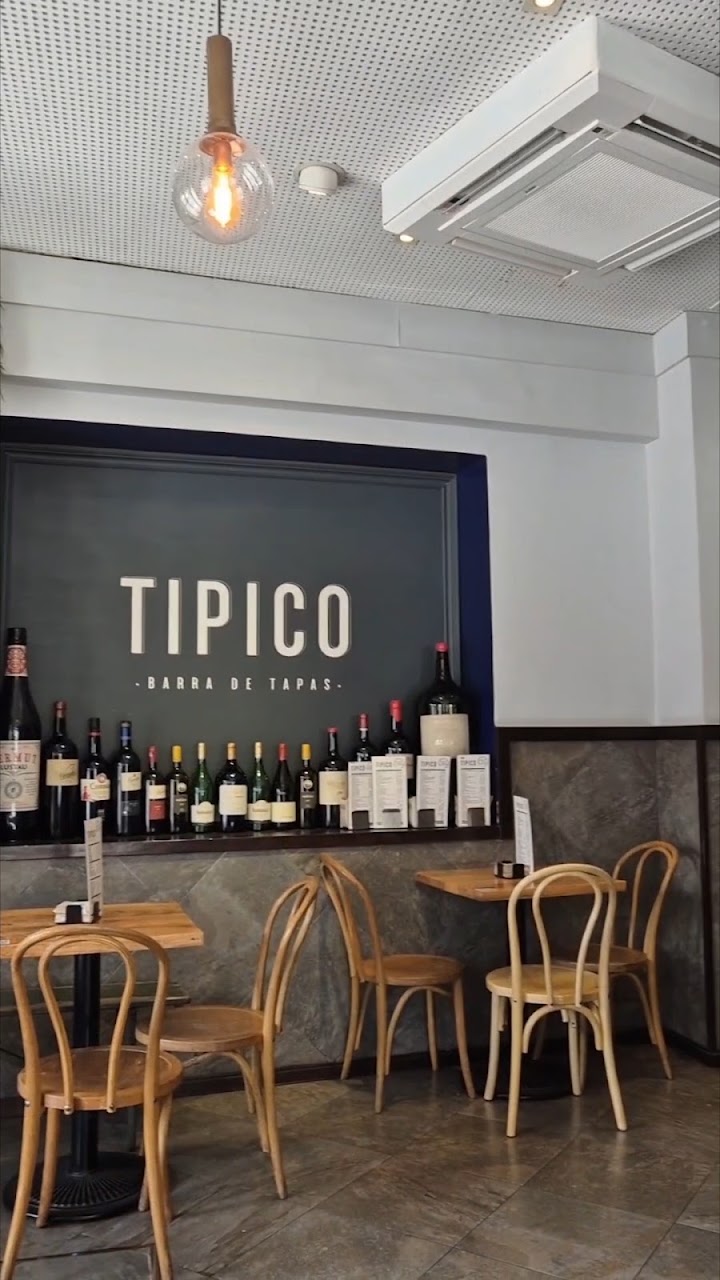 Interior del bar con el rótulo Típico en la pared, botellas de vino y mesas altas